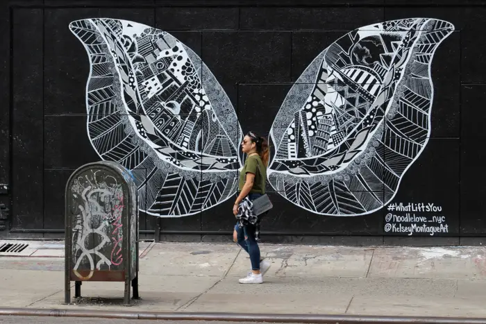 A photo of a person walking in front of butterfly wing graffiti in Nolita